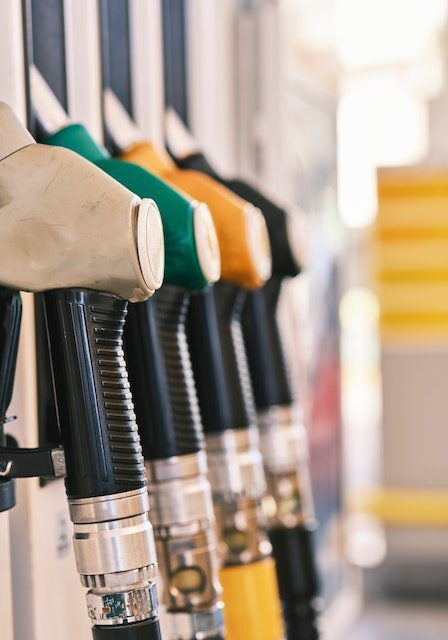 A row of fuel pump nozzles with different colored handles at a gas station.