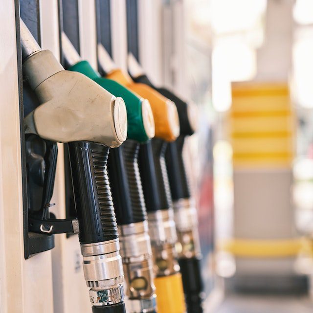 A row of fuel pump nozzles with different colored handles at a gas station.