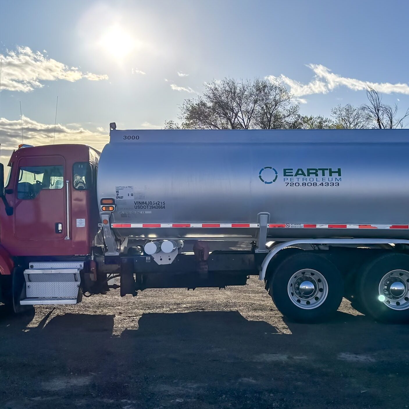 A red fuel delivery truck labeled "Earth Petroleum" is parked outdoors with trees and a bright sun in the background.
