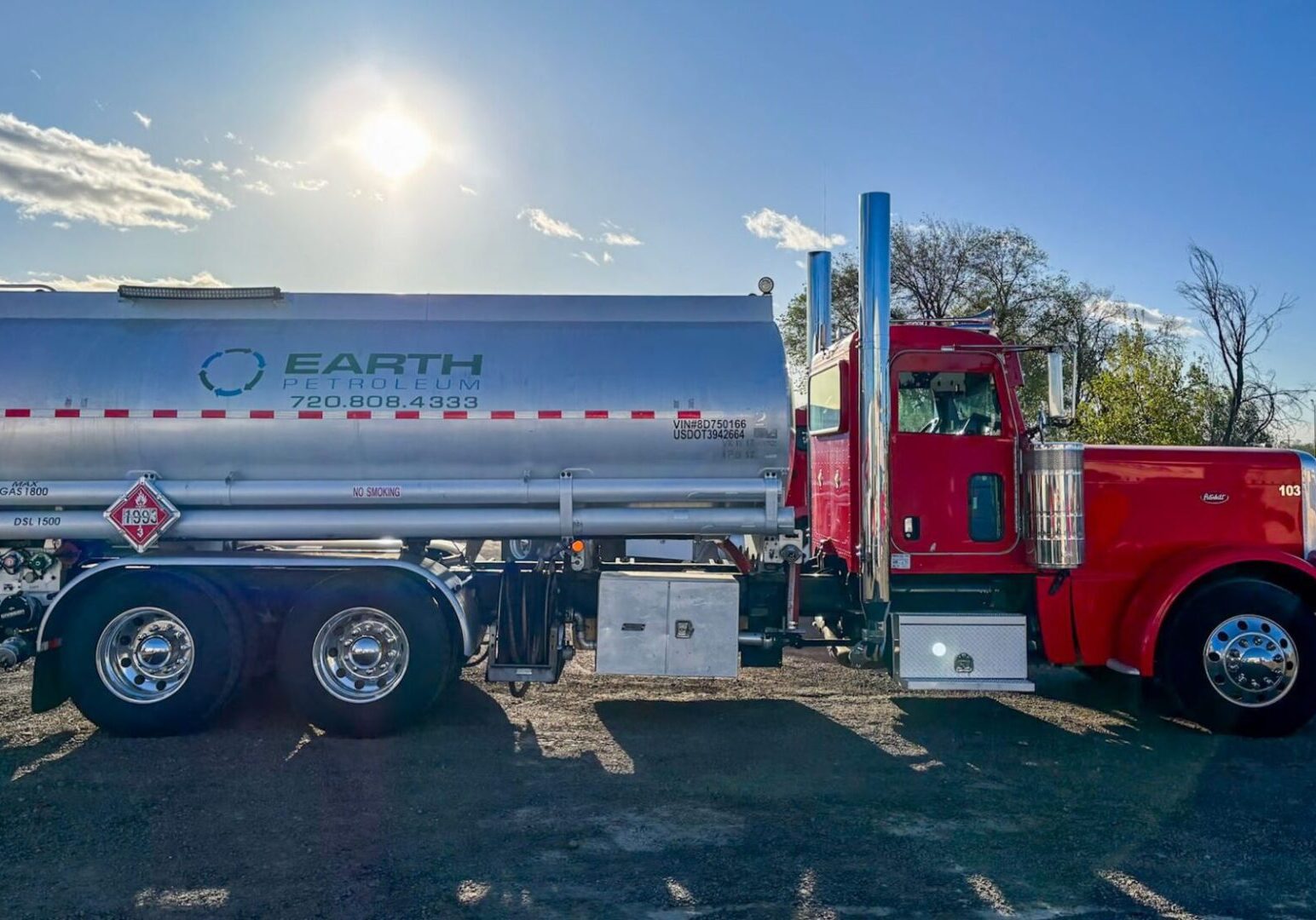 A red fuel tanker truck labeled "Earth Petroleum" is parked outdoors on a sunny day, with trees and a building in the background.